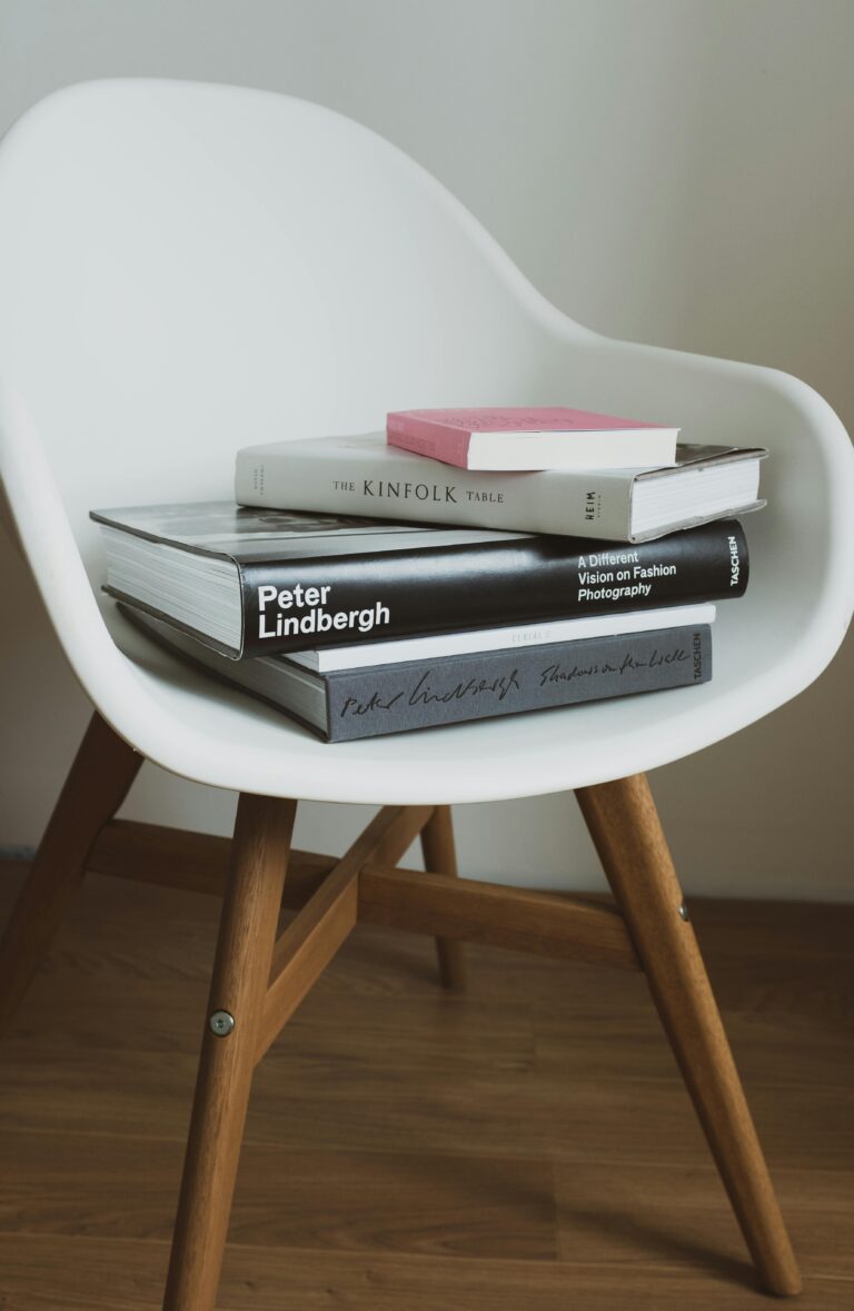 Comfortable white chair with stack of various books placed near wall in light modern room of cozy home